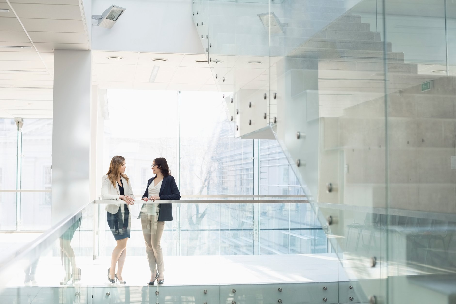 Businesswomen conversing against railing in office